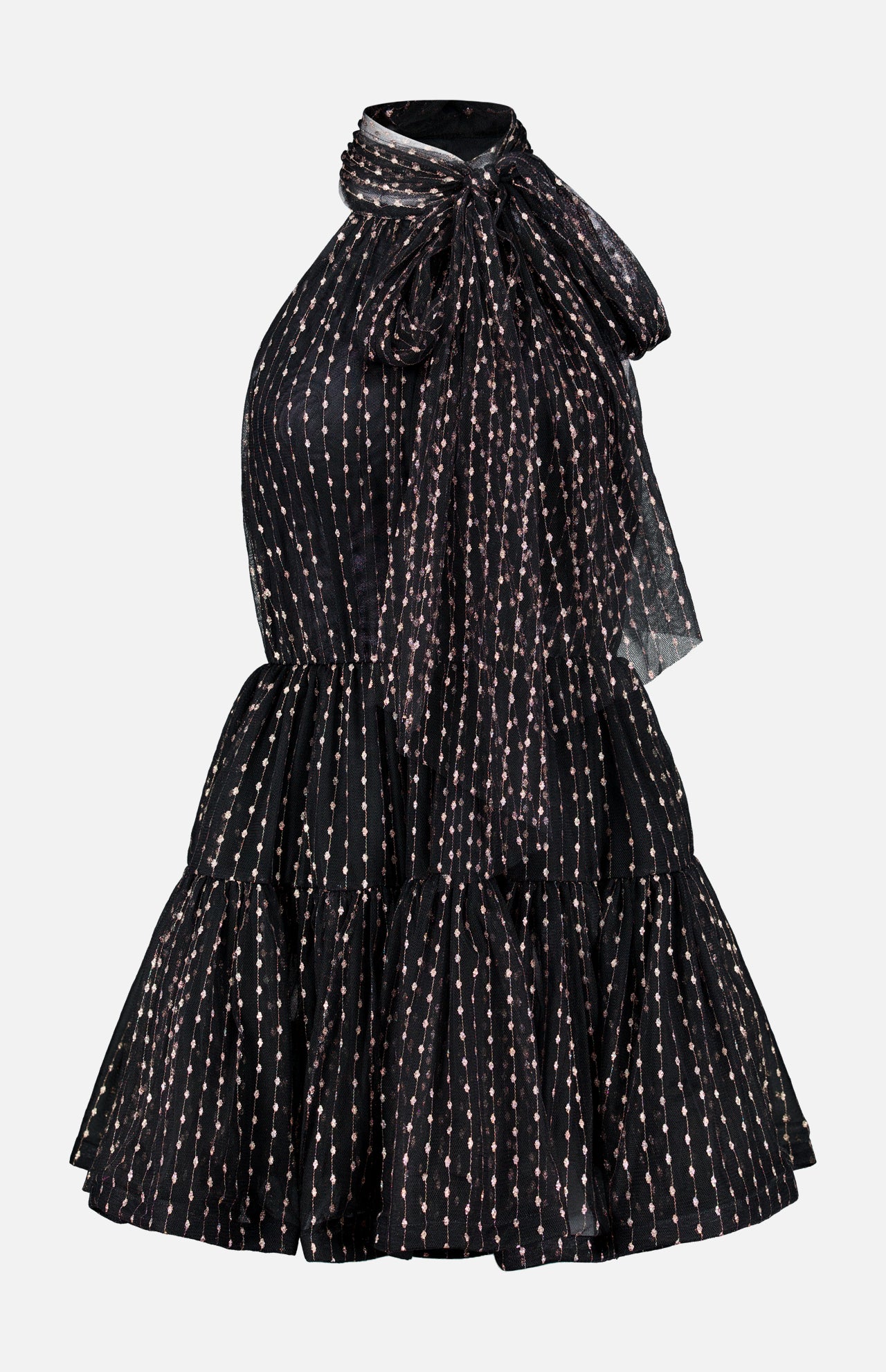 The Olga Tulle Short Dress by PATBO is a black sleeveless mini dress with a halter neckline, highlighted by a statement bow at the neck and a tiered, ruffled skirt. Its tulle fabric features vertical rows of small, light-colored dots for a touch of playful elegance.