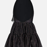 The Olga Tulle Short Dress by PATBO is a sleeveless black mini dress with a halter neckline and an open back, featuring a flared, tiered skirt decorated with small, light-colored dotted lines.