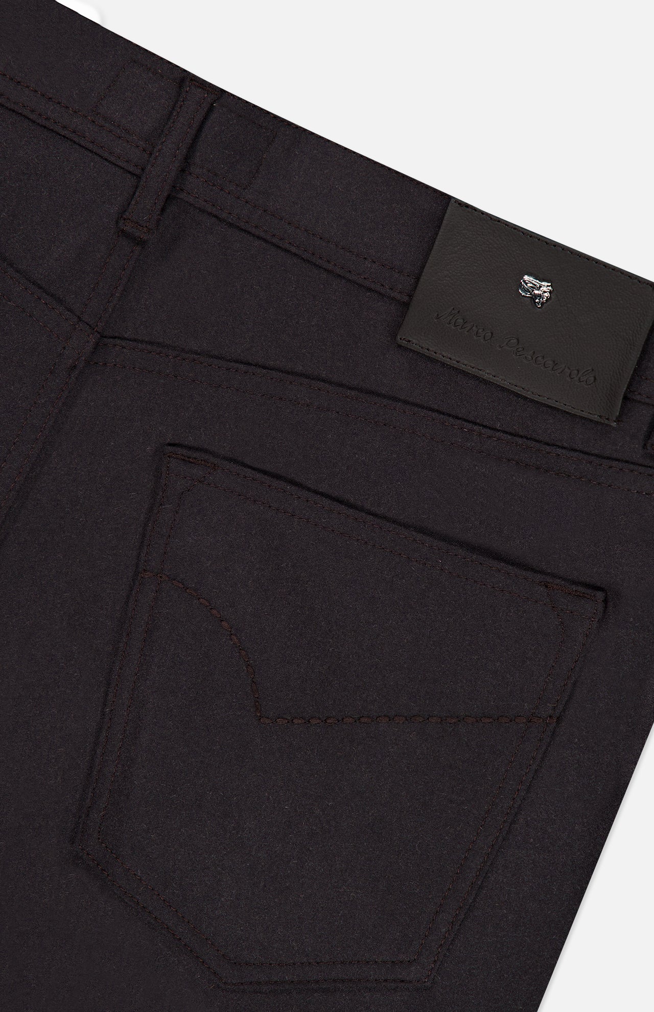 Close-up of the back pocket and waistband of the PESCAROLO Nerano M Cashmere Pants in a dark hue, highlighting intricate stitching details and a black leather patch adorned with embossed text and a small metallic emblem. This 5-pocket design exemplifies refined craftsmanship and premium quality, characteristic of pieces made in Italy.