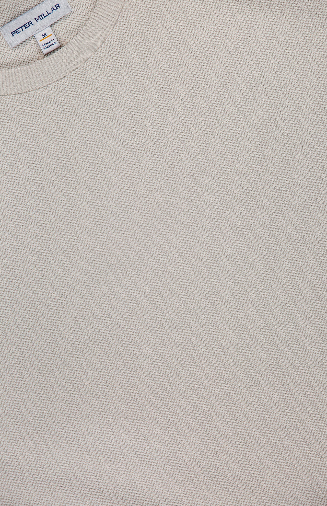 Close-up of the Cradle Pique Performance Long Sleeve Sweatshirt by PETER MILLAR in light beige, featuring textured piqué fabric and the visible brand label at the neckline. Size: medium. Made in India.