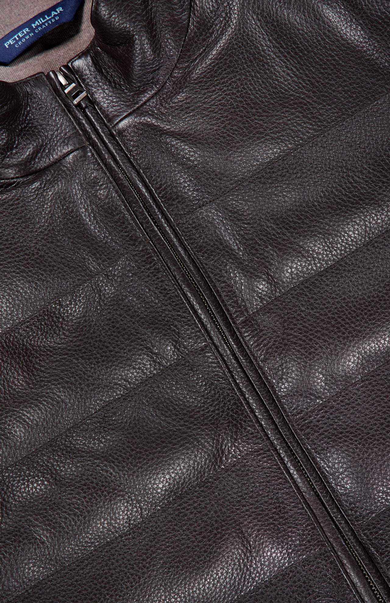 Close-up of a dark brown textured Deerskin Leather Vest with a visible zipper and PETER MILLAR label on the inside collar, featuring merino wool lining for added comfort—an exceptional choice in luxury outerwear.