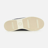 The image shows the beige rubber sole of the PETER MILLAR Drift Classic Nubuck Sneaker, viewed from below. The design features three horizontal grooves—two at the front and one at the heel—with a circular logo centered in the sole.