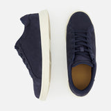 The image displays the PETER MILLAR Drift Classic Nubuck Sneaker in men's navy, featuring white soles. One shoe is shown from the side and the other from above, set against a plain light background.