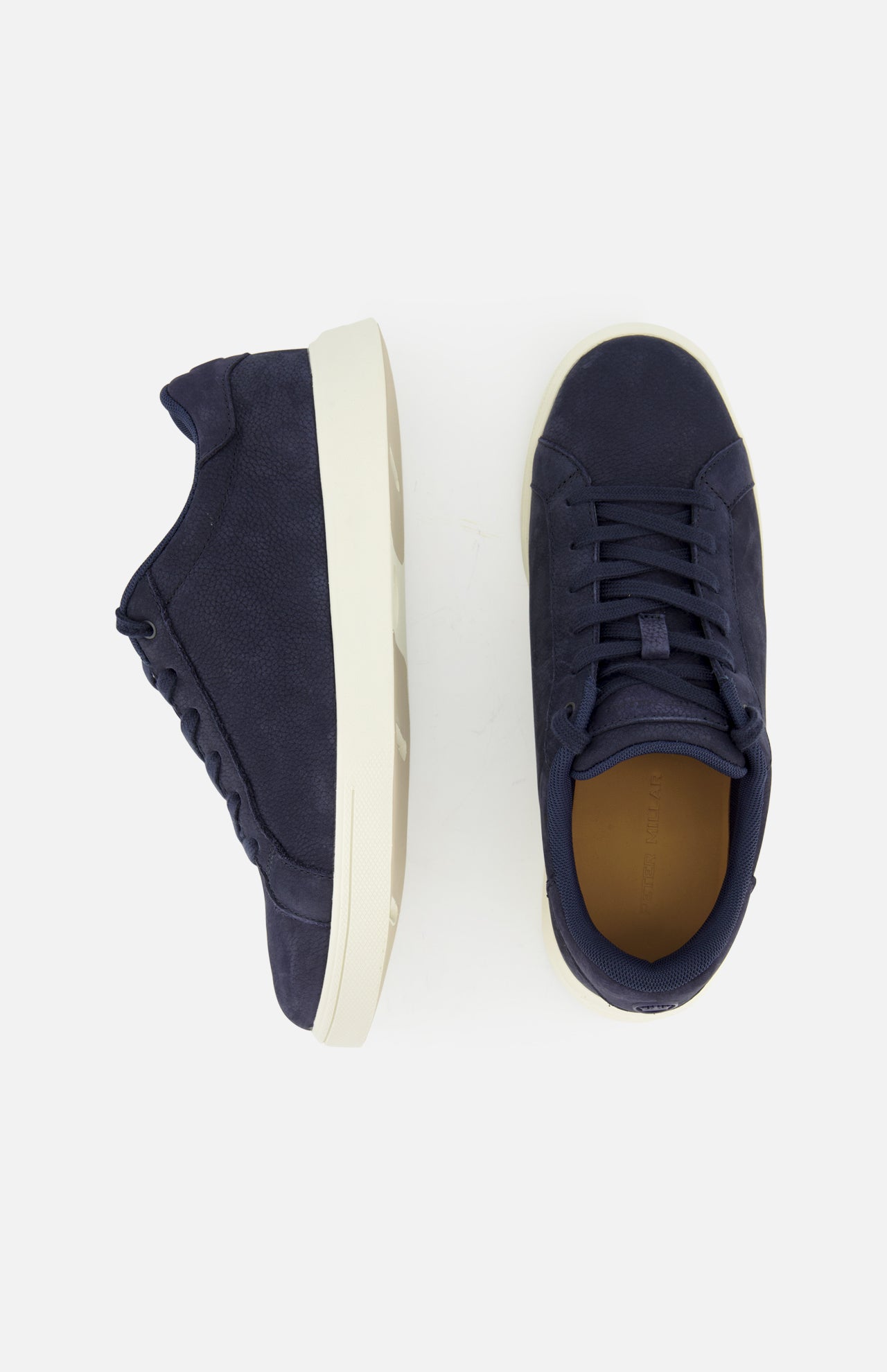 The image displays the PETER MILLAR Drift Classic Nubuck Sneaker in men's navy, featuring white soles. One shoe is shown from the side and the other from above, set against a plain light background.