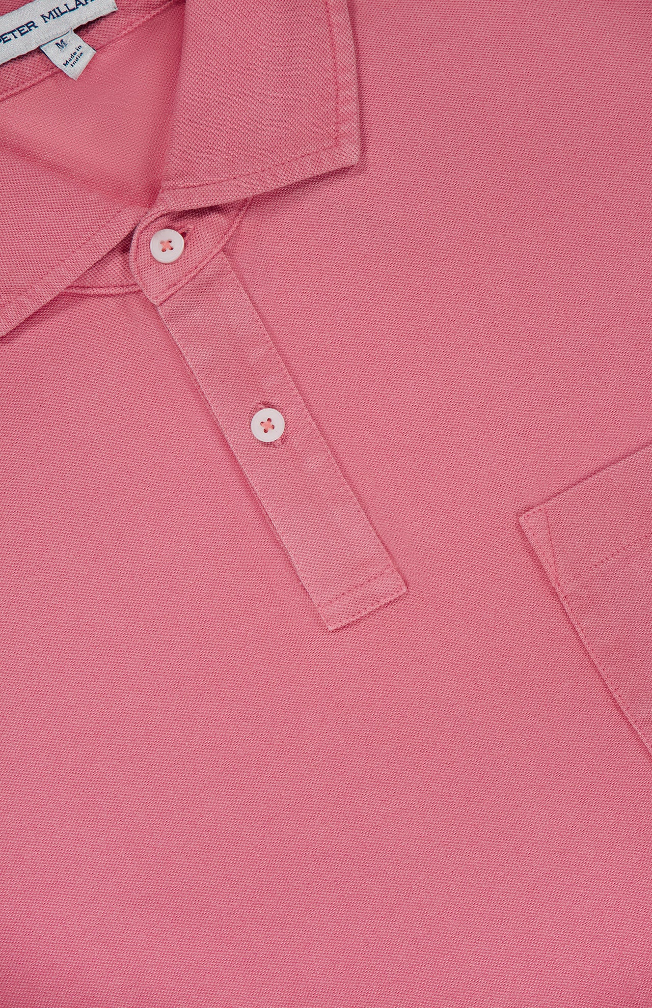 Close-up of the PETER MILLAR Everyday Pique Polo Shirt in pink organic cotton, featuring two buttons, a chest pocket, and detailed fabric texture with part of the collar and placket visible.