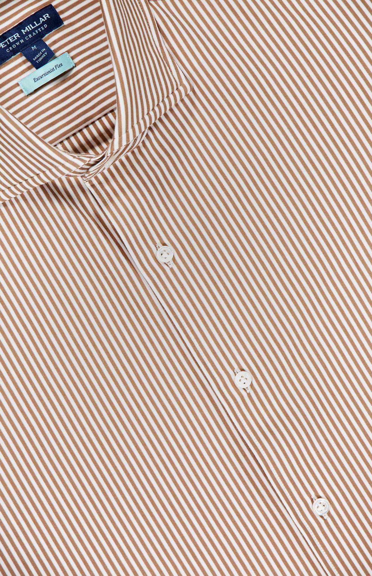 A close-up of the PETER MILLAR Excursionist Flex Stripe Sport Shirt showcases its brown fabric with white vertical stripes, white buttons, and a blue label inside the collar. Crafted from wrinkle-resistant, cotton-stretch material, this shirt provides both comfort and easy care.
