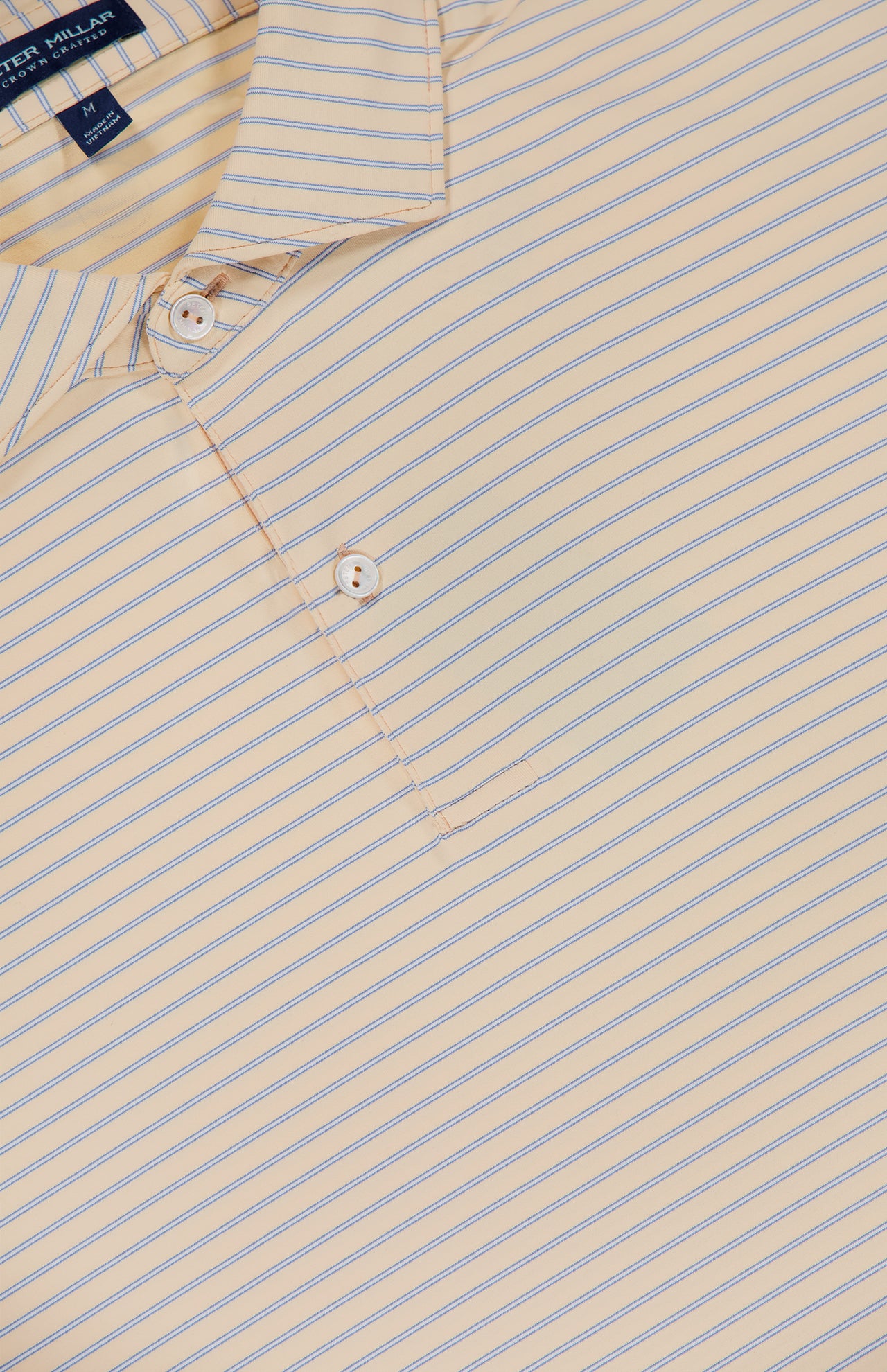 A close-up of the PETER MILLAR Keynote Performance Jersey Polo Shirt in light yellow with thin blue diagonal stripes, featuring a two-button placket, moisture-wicking UPF 50+ fabric, and a slightly visible shirt tag at the top left.