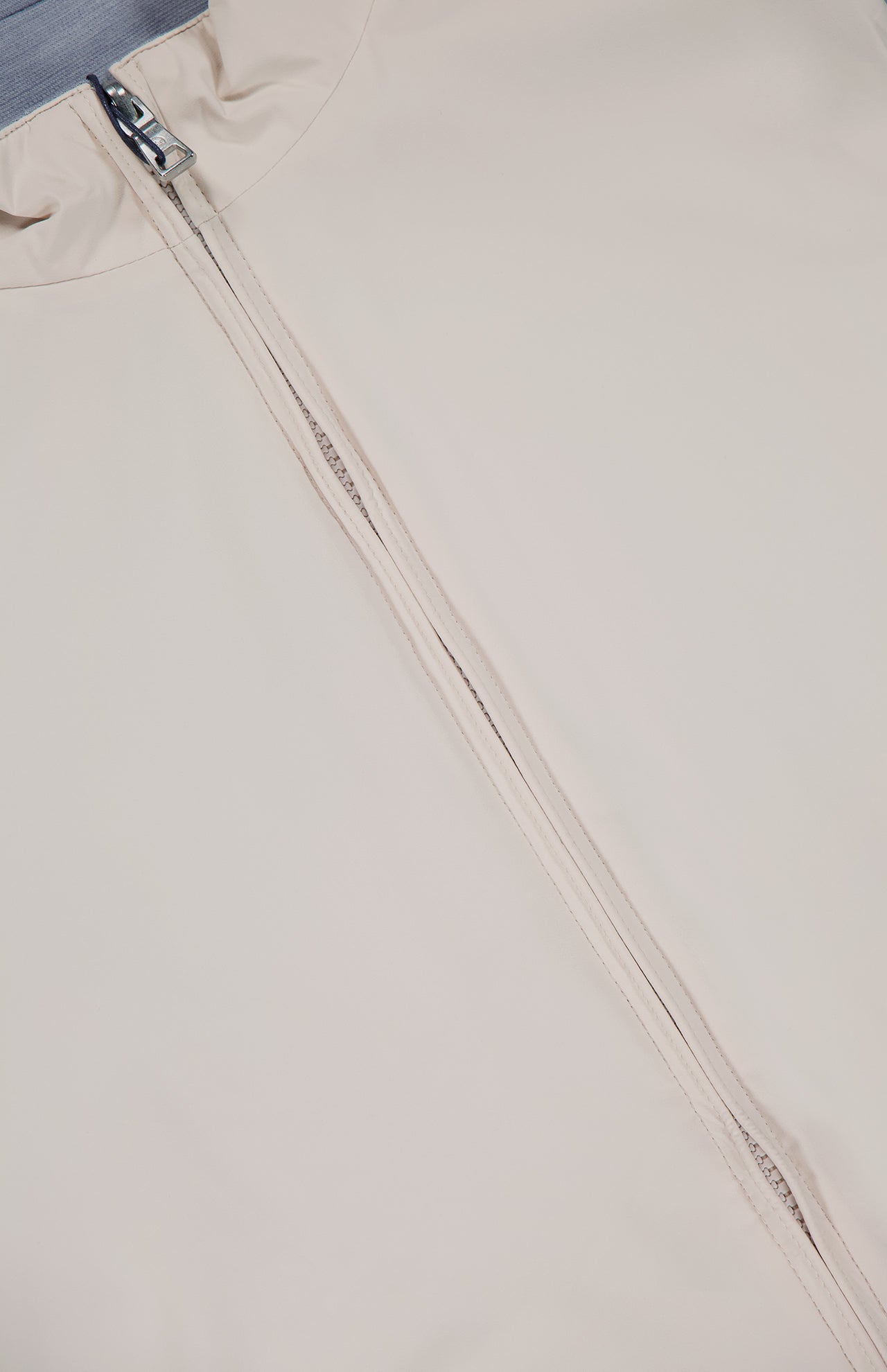 A close-up of the PETER MILLAR Ryder Reversible Water Resistant Vest in light beige shows the partially unzipped front silver zipper, with part of the collar and smooth, soft fabric visible on both sides.