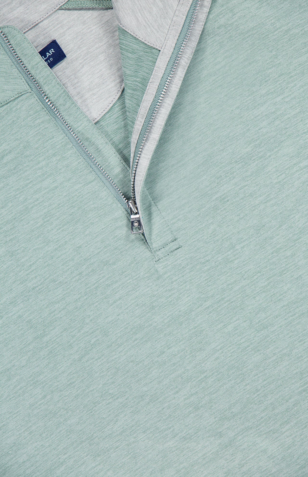 Close-up of the PETER MILLAR Stealth Performance Quarter-Zip Pullover in light green, featuring a silver zipper, light grey inner lining, blue label, moisture-wicking fabric, and UPF 50+ sun protection.