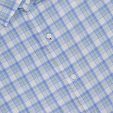 A close-up of the PETER MILLAR Waterrock Cotton Lyocell Sport Shirt in light blue, green, and white plaid, featuring part of the collar, three white buttons, and the brand label. Made from stretch performance fabric for comfort.