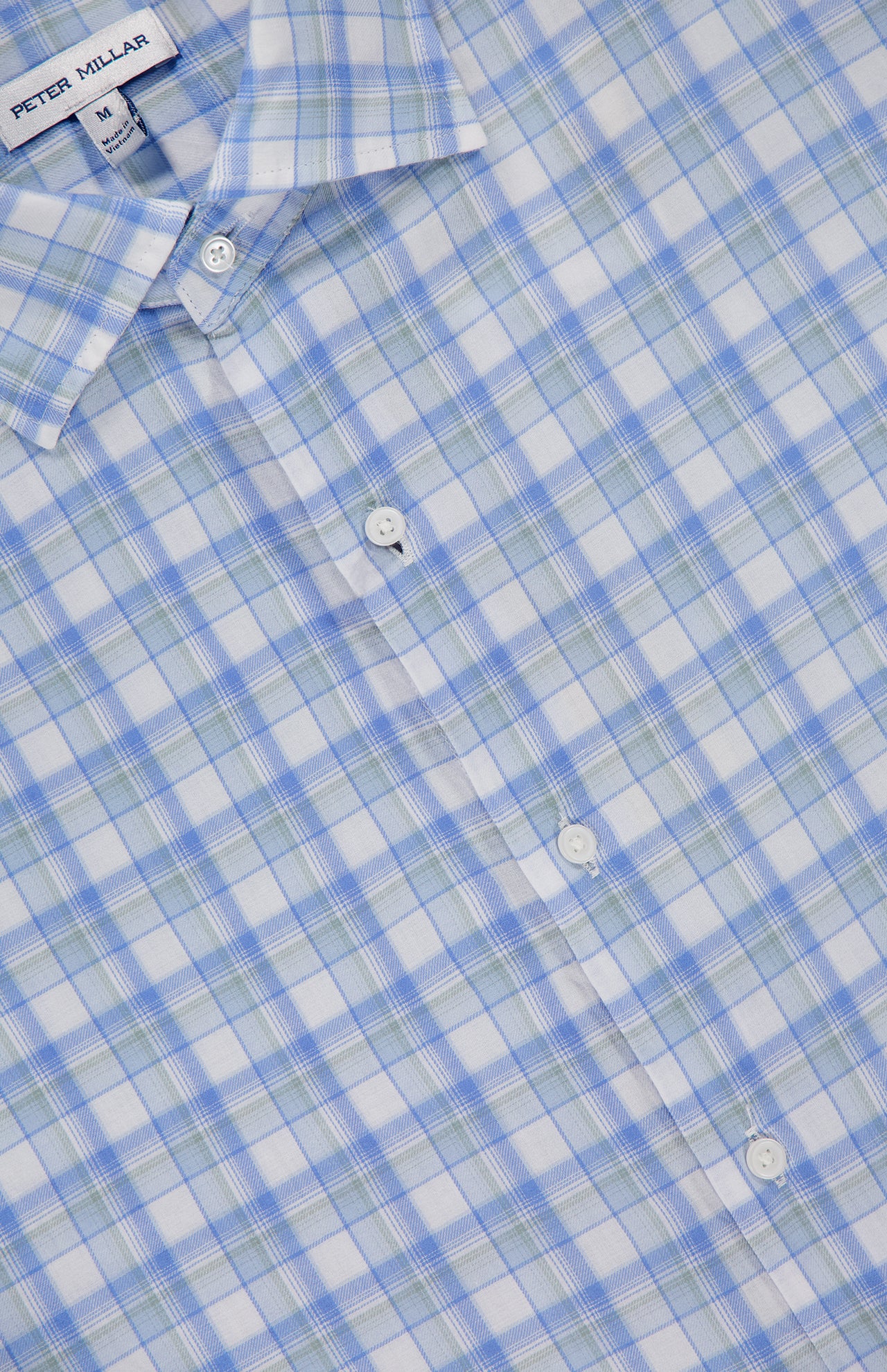 A close-up of the PETER MILLAR Waterrock Cotton Lyocell Sport Shirt in light blue, green, and white plaid, featuring part of the collar, three white buttons, and the brand label. Made from stretch performance fabric for comfort.