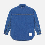 The Oversized Denim Shirt Jacket by 3.1 PHILLIP LIM is a long-sleeved blue jean shirt with a collar, silver cuff buttons, silver studs near the collar, and a white rectangular patch above the bottom hem, shown from the back.