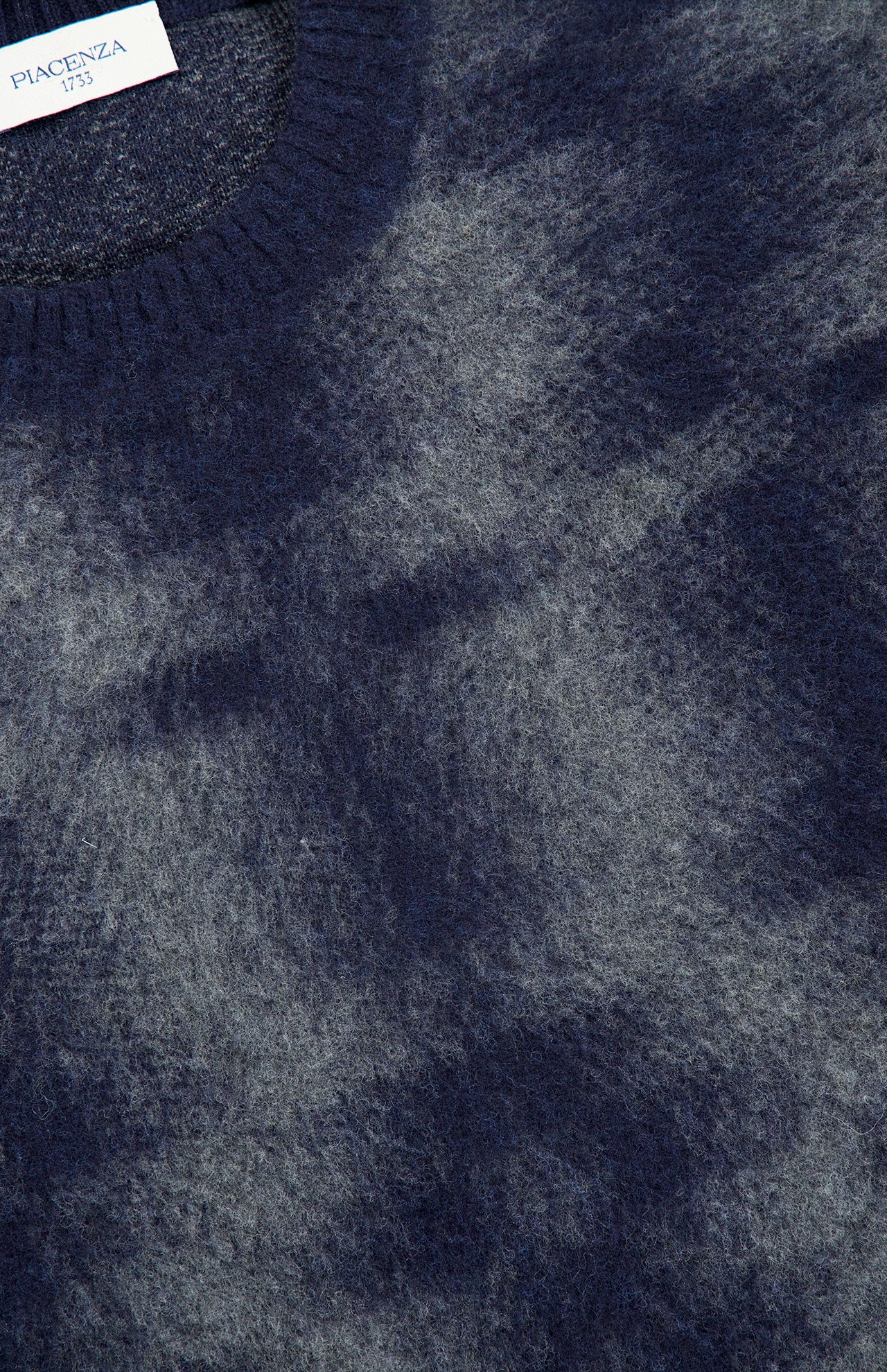 Close-up of a soft, fuzzy blue Combed Pixel Stripe Crewneck Sweater in virgin wool with a rounded neckline. A white PIACENZA label is partially visible at the top left corner.
