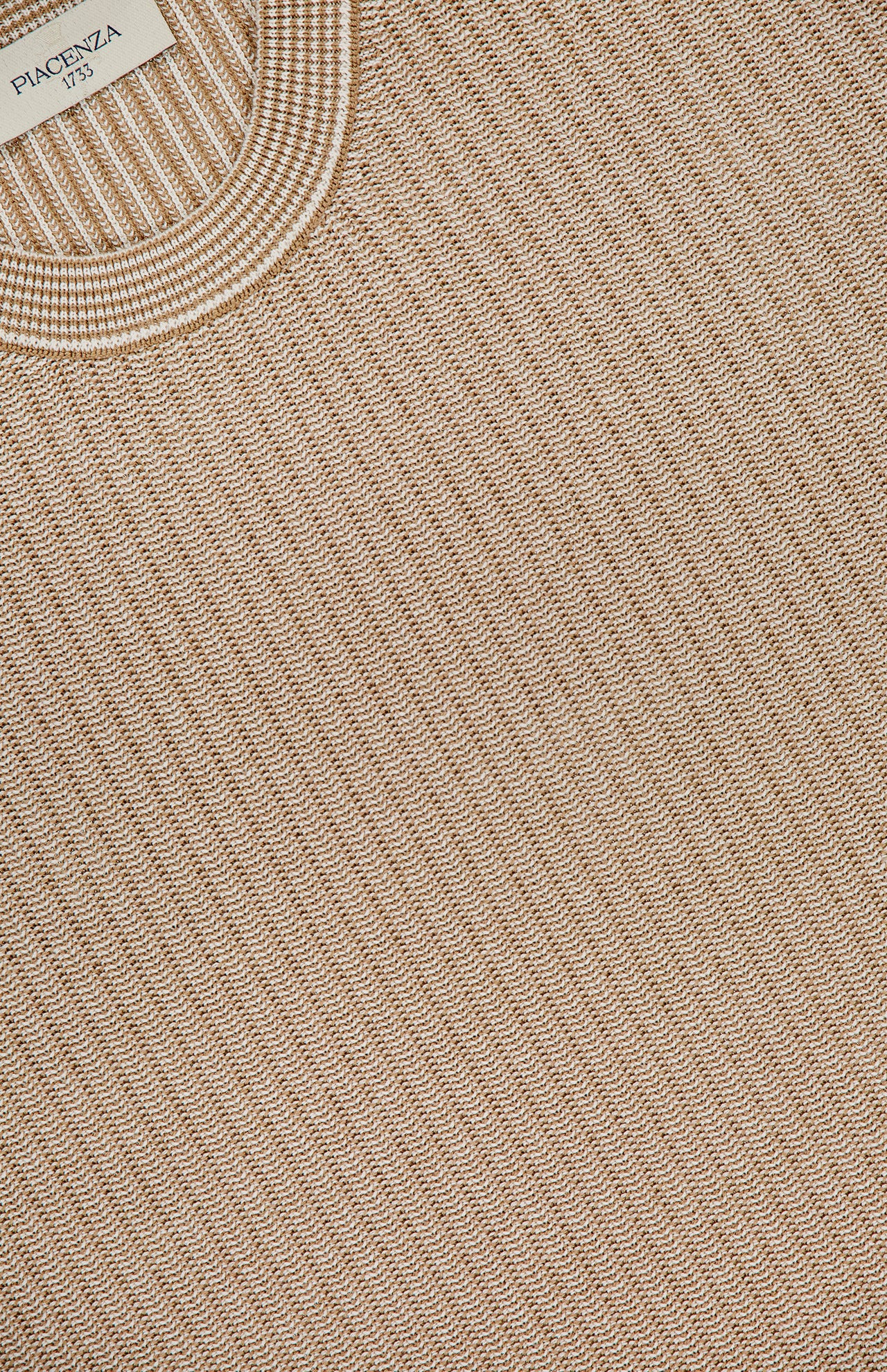 Close-up of the PIACENZA Crewneck Short Sleeve Knit Sweater in tan silk cotton, featuring rib-knit texture, round neckline, detailed craftsmanship, and a visible label near the collar. Expertly made in Italy.