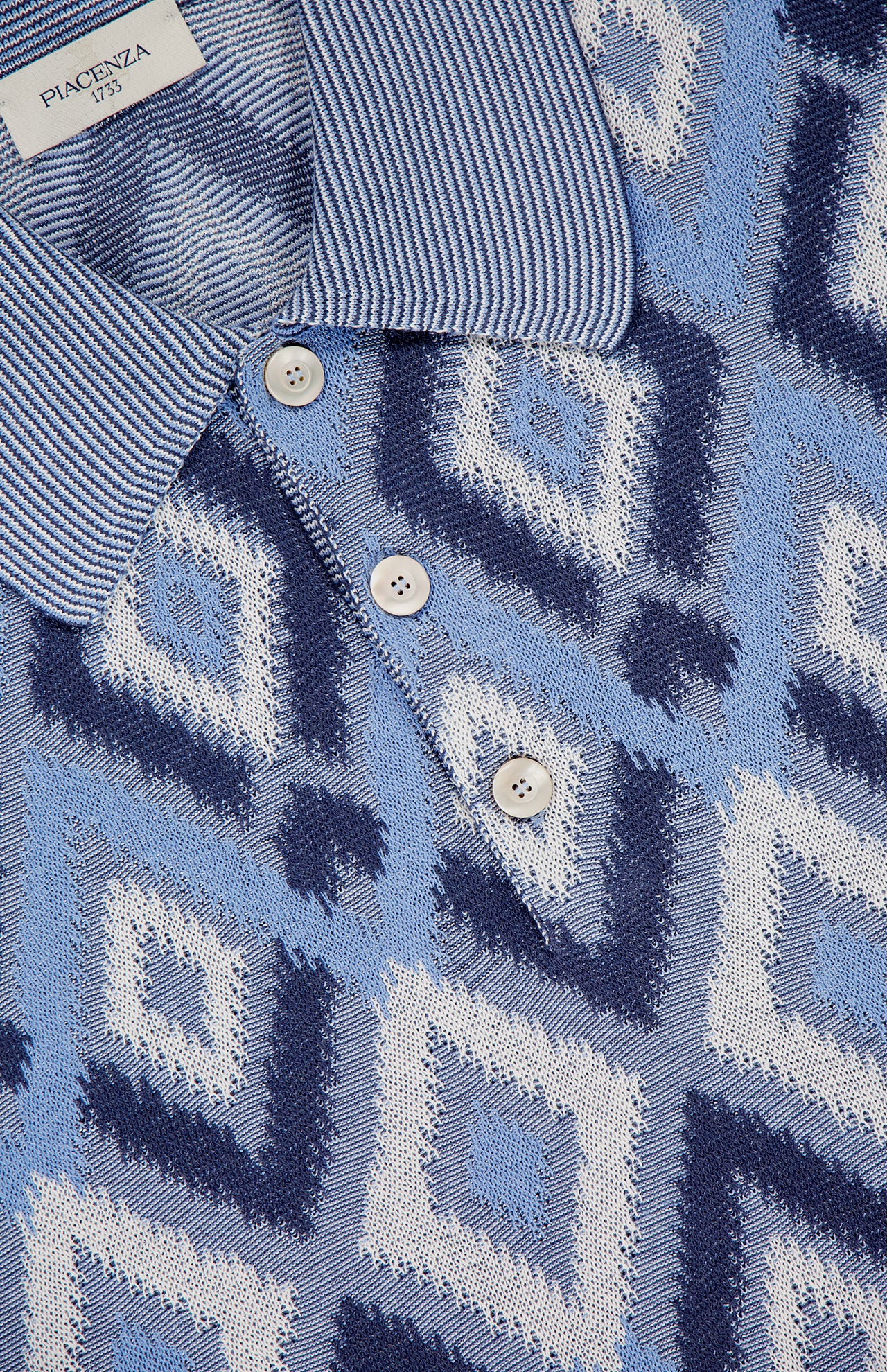 Close-up of the PIACENZA Diamond Shaped Print Knit Polo Shirt in navy, made in Italy, with blue and white geometric diamonds, striped collar, three buttons, and a visible Piacenza 1733 label.
