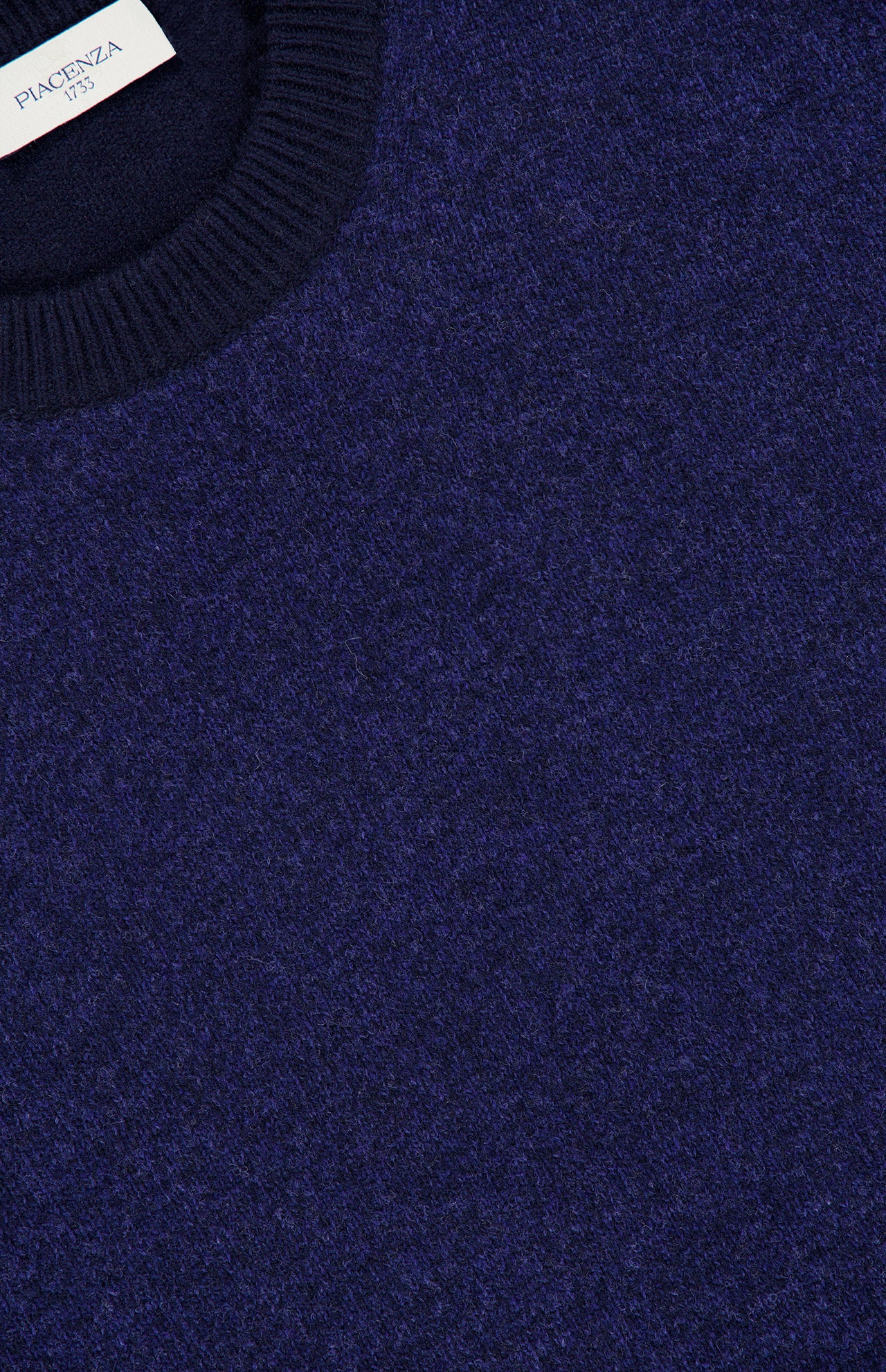 Close-up of a Solid Mouliné Color Block Crewneck Sweater with a ribbed collar. A white PIACENZA label is inside the neckline. The sweater’s soft, slightly fuzzy texture is crafted in Italy.