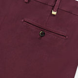 Close-up of the Stretch Overdyed Solaro Trouser Pant by PT TORINO in burgundy, showcasing a back pocket with a single button and a gold metal accent near the waistband. Crafted from a cotton-blend fabric with a subtle diagonal texture, these trousers are an ideal option for professional attire.
