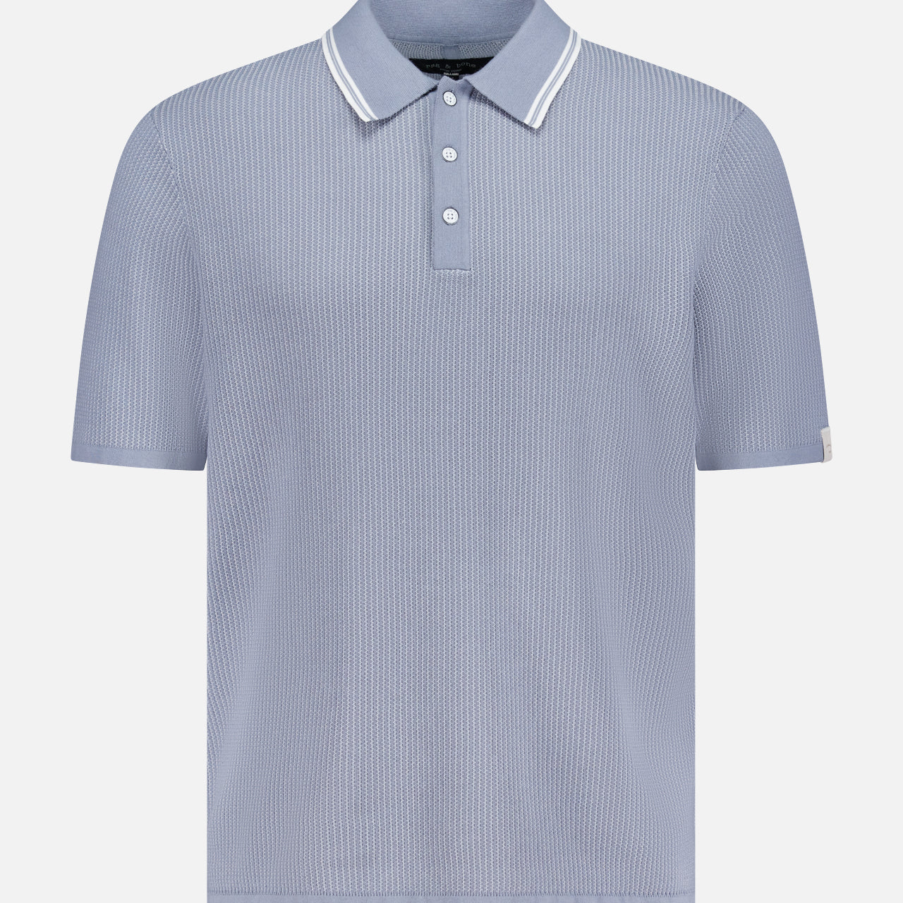 The RAG & BONE Harvey Tipped Polo Shirt features lightweight cotton in pale blue, a ribbed texture, white-trimmed collar, three-button placket, and subtle vertical stripes. Displayed on a plain white background.