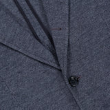 Close-up of the Becker Knit Sportcoat by RAG & BONE, featuring dark grey lightweight cotton-blend fabric with a subtle pattern. The image highlights the lapel, two buttons, and part of a pocket, with visible stitching along the edges that reflect its British sport coat-inspired design.