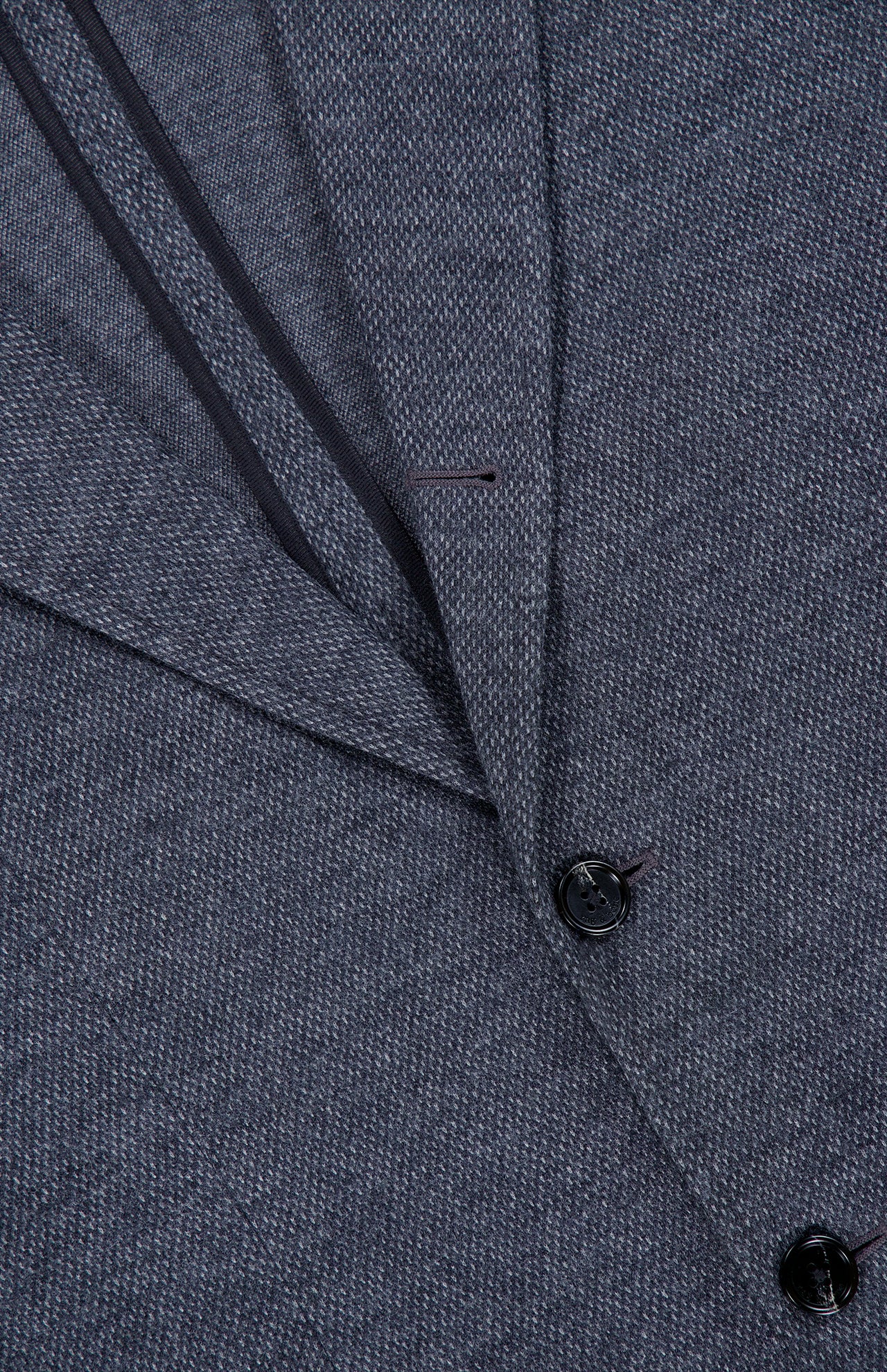 Close-up of the Becker Knit Sportcoat by RAG & BONE, featuring dark grey lightweight cotton-blend fabric with a subtle pattern. The image highlights the lapel, two buttons, and part of a pocket, with visible stitching along the edges that reflect its British sport coat-inspired design.