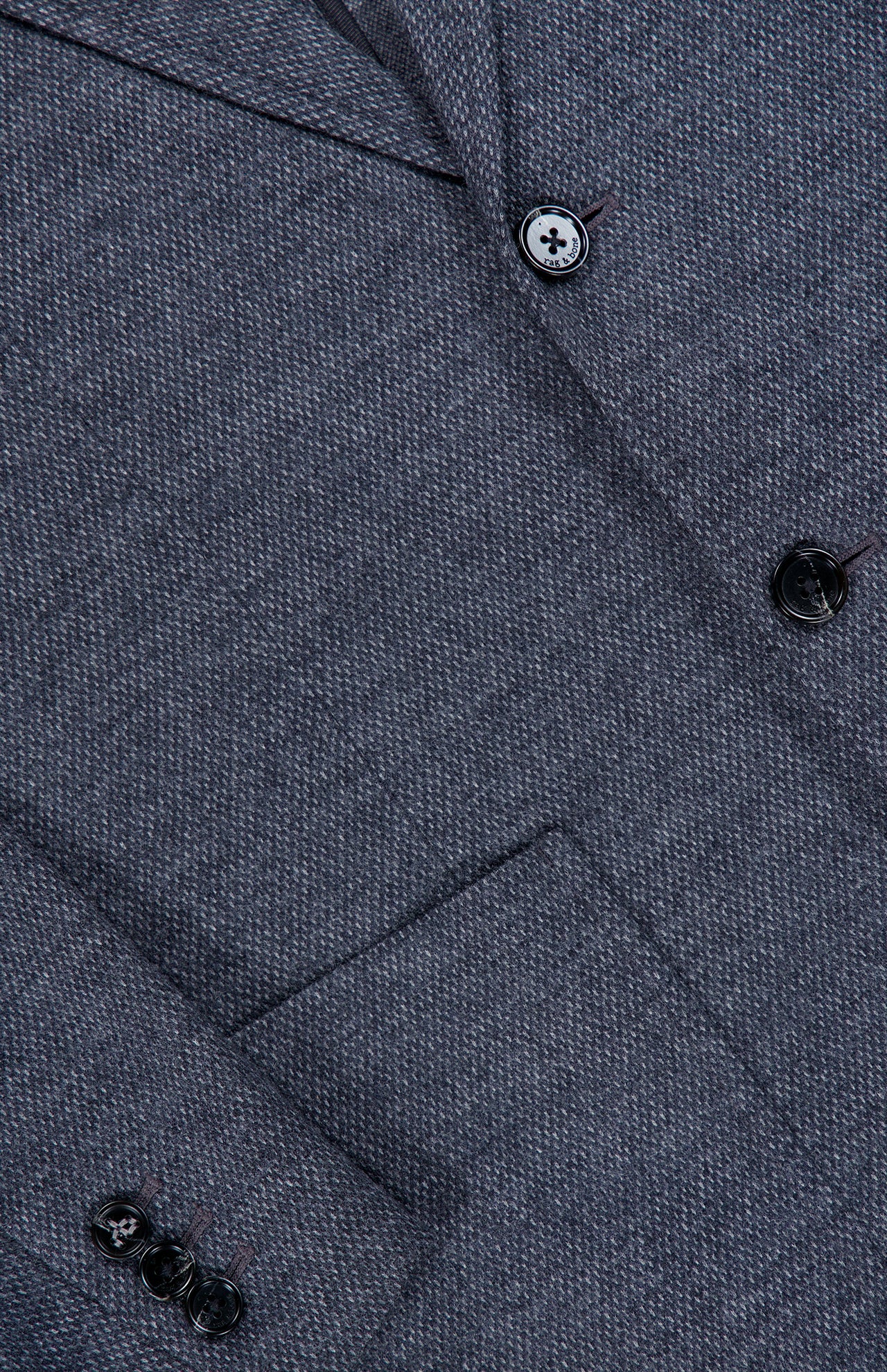 Close-up of the RAG & BONE Becker Knit Sportcoat in dark grey, featuring a herringbone pattern crafted from lightweight cotton-blend fabric, with details including a front pocket, sleeve buttons, and part of the lapel.