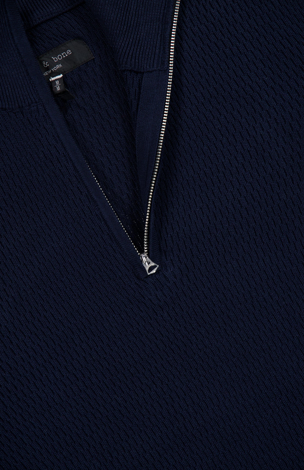 Close-up of the Danton Cotton Quarter Zip Sweater by RAG & BONE in navy, featuring a textured knit and a silver half-zipper partially unzipped with a black label visible inside the collar.