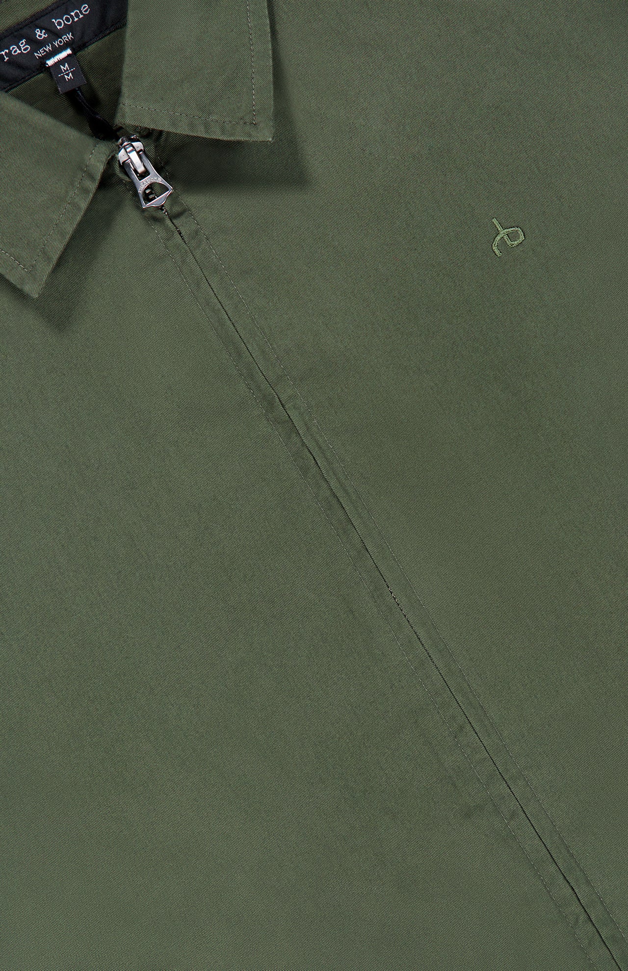 Close-up of the olive green Harrington Cotton Jacket by RAG & BONE, featuring a classic collared design with a zipper and a subtle embroidered logo on the chest, inspired by traditional British sportswear. The RAG & BONE tag is partially visible near the collar.