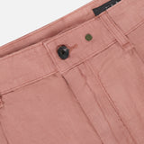 Close-up of the waistband and top front of the Jackson Pleated Linen Short by RAG & BONE in light pink, featuring a black button, metal rivet, belt loops, and visible stitching for a classic look.