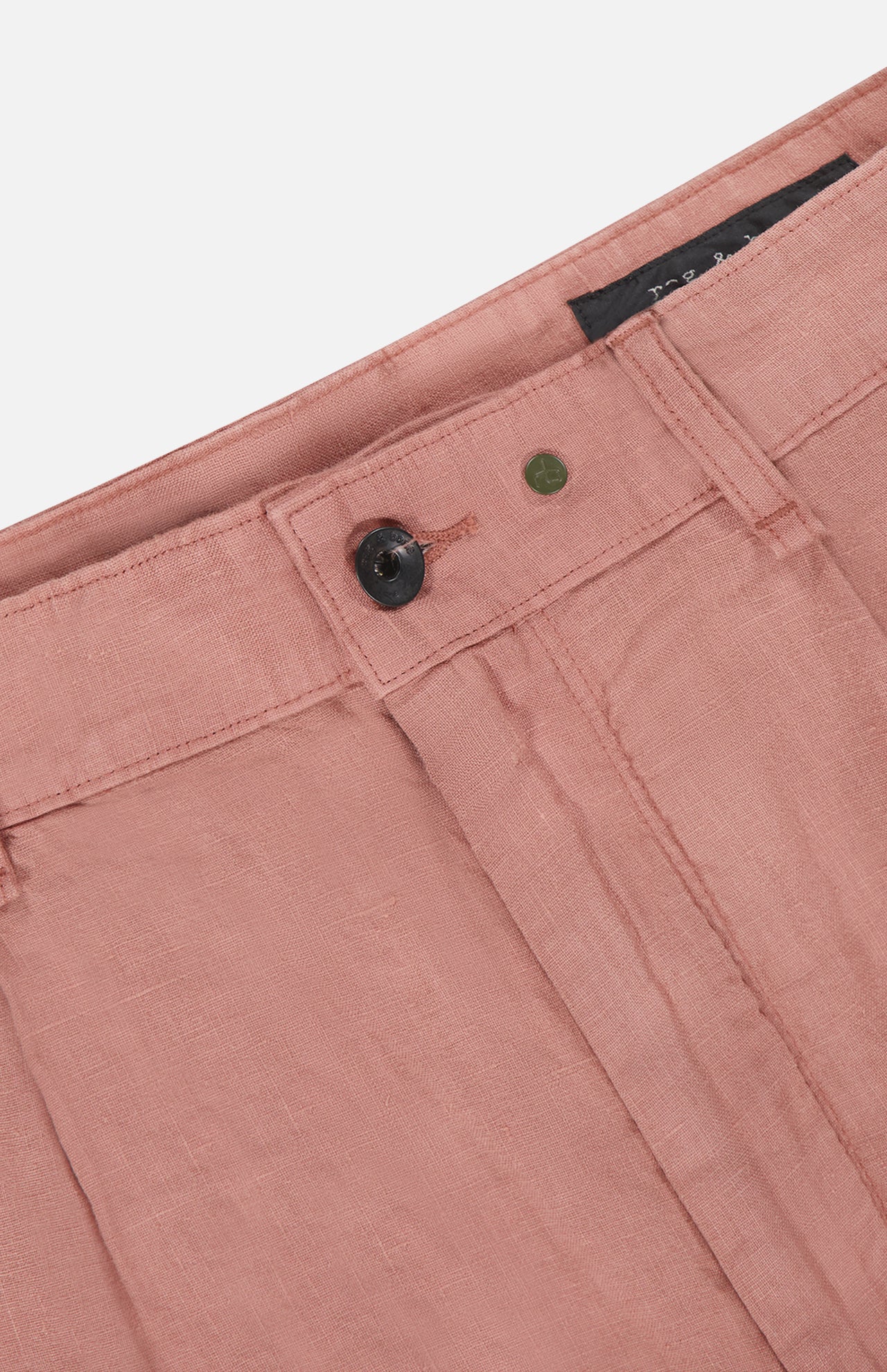 Close-up of the waistband and top front of the Jackson Pleated Linen Short by RAG & BONE in light pink, featuring a black button, metal rivet, belt loops, and visible stitching for a classic look.