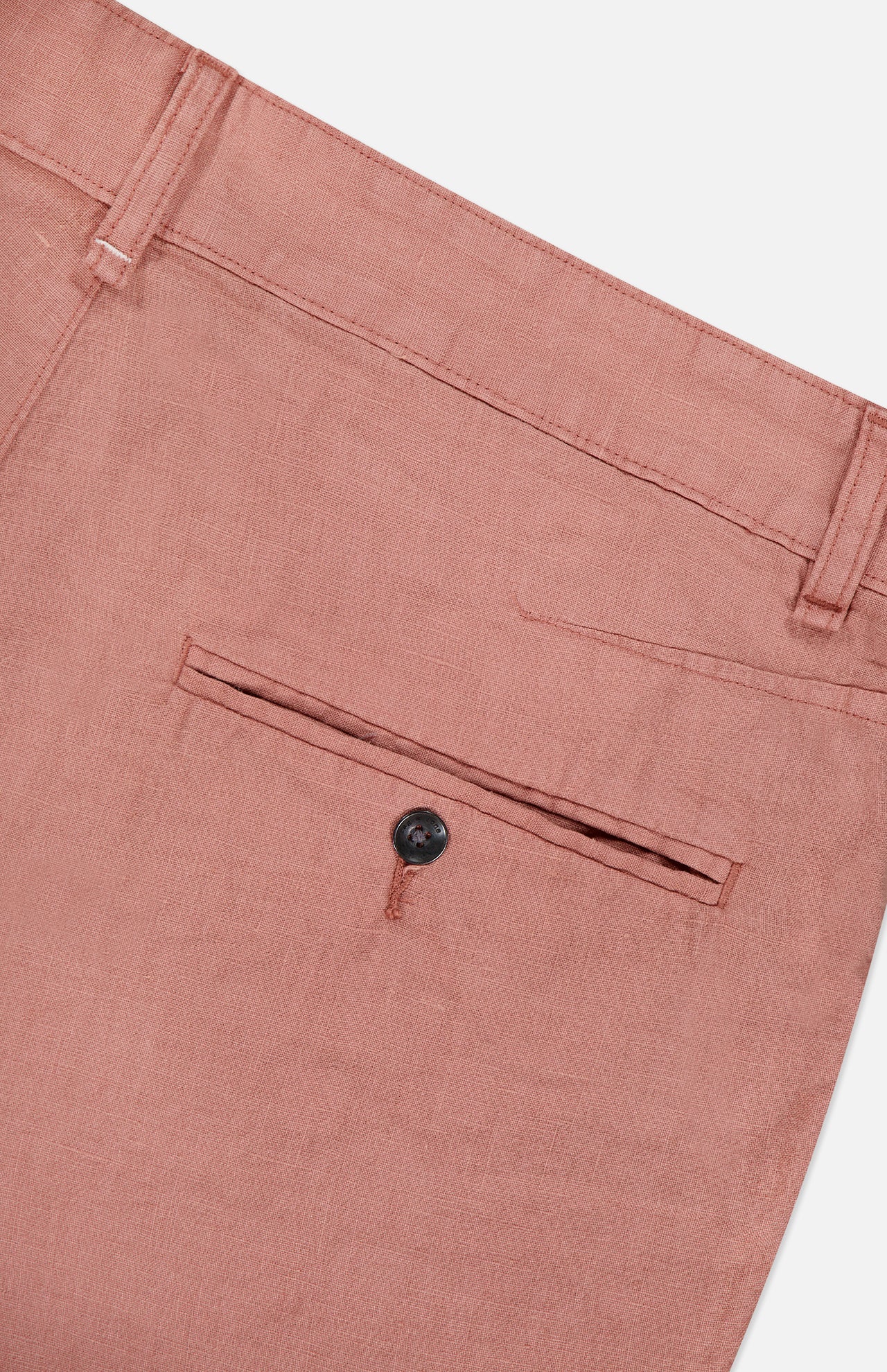 Close-up of the back of the RAG & BONE Jackson Pleated Linen Short, featuring a single welt pocket with a dark button and belt loops along the waistband. Shown in light brown or dusty rose classic fit linen.