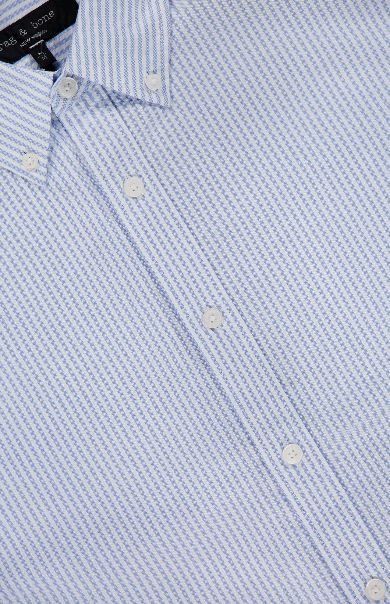 Close-up of the RAG & BONE RB Classic Striped Oxford Shirt, showcasing blue stripes, white buttons, a button-down collar, diagonal fabric pattern, and a partial shirt label visible at the top left.