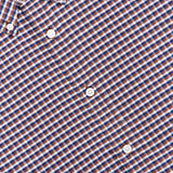 Close-up of the RAG & BONE Classic Oxford Dress Shirt, crafted from 100% cotton with a small brown and navy check pattern accented by white. Crisp white buttons and a structured collar are also visible in the upper left corner.