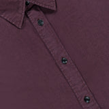 A close-up of the Tomlin Dobby Dress Shirt by RAG & BONE, a burgundy stretch cotton button-up with black buttons and a pointed collar, displayed on a flat surface. The shirt tag displays the brand name RAG & BONE.