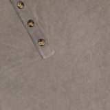 Close-up of the RAG & BONE Washed Cotton Henley Shirt in beige, featuring soft cotton yarn, a partial view of the collar, and four brown buttons along the placket on a textured fabric background.