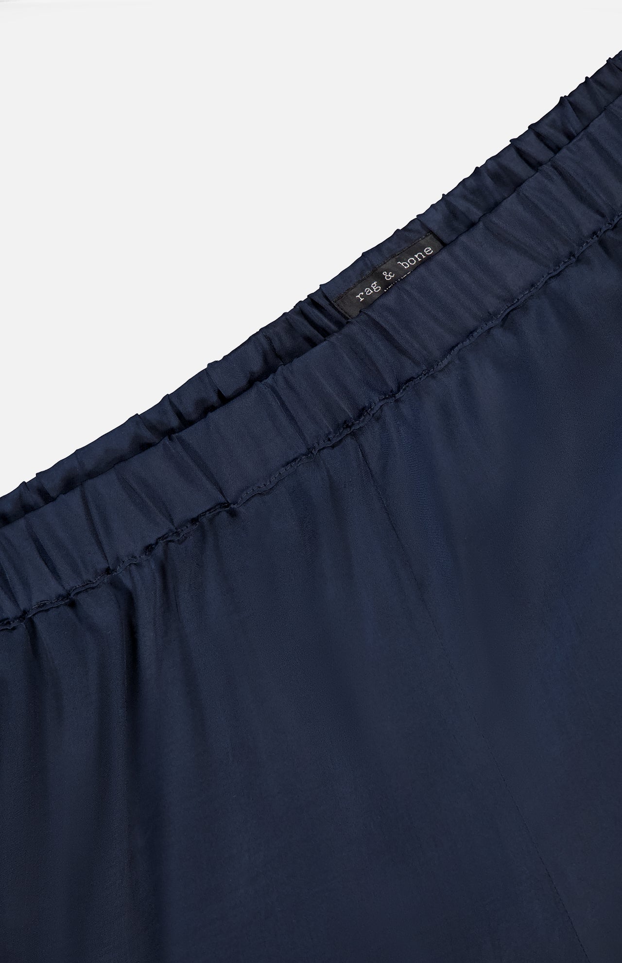 Close-up of the waistband of the Olivia Contrast Stripe Pant by RAG & BONE, featuring a relaxed fit, elastic band, and visible black brand label. The smooth navy fabric appears lightweight.