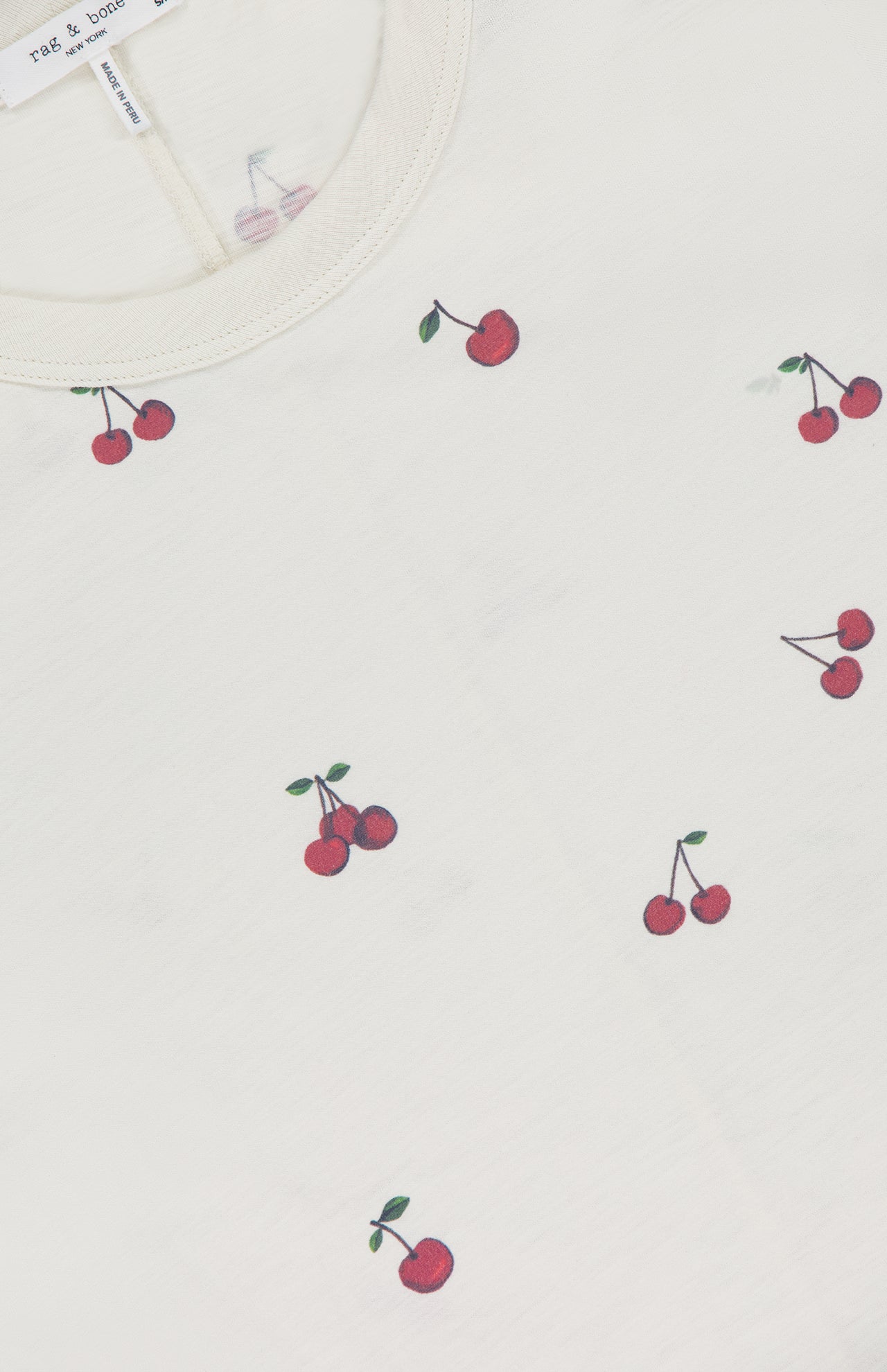 A close-up of the RAG & BONE All Over Cherry T-shirt in white Peruvian cotton, featuring a playful cherry print with small red cherries throughout and a visible collar label.