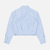 The Andy Pleated Drawcord Top by RAG & BONE is a light blue, long-sleeve cropped shirt with a collared neckline and buttoned cuffs, shown from the back on a white background. This cotton blouse brings a modern edge to the classic button-down.