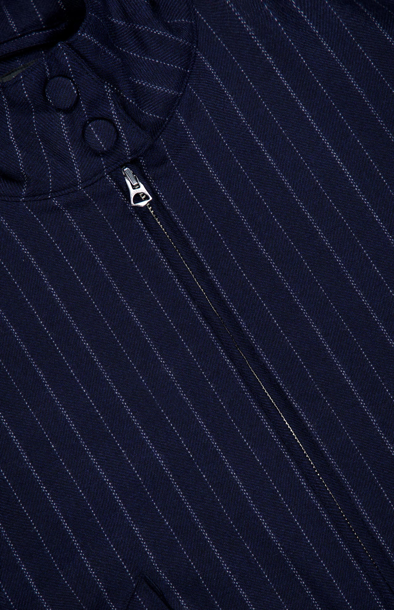 Close-up of the Eliza Striped Bomber Jacket by RAG & BONE, featuring navy blue pinstripe fabric, a vertical silver zipper, and two fabric-covered buttons near the collar.