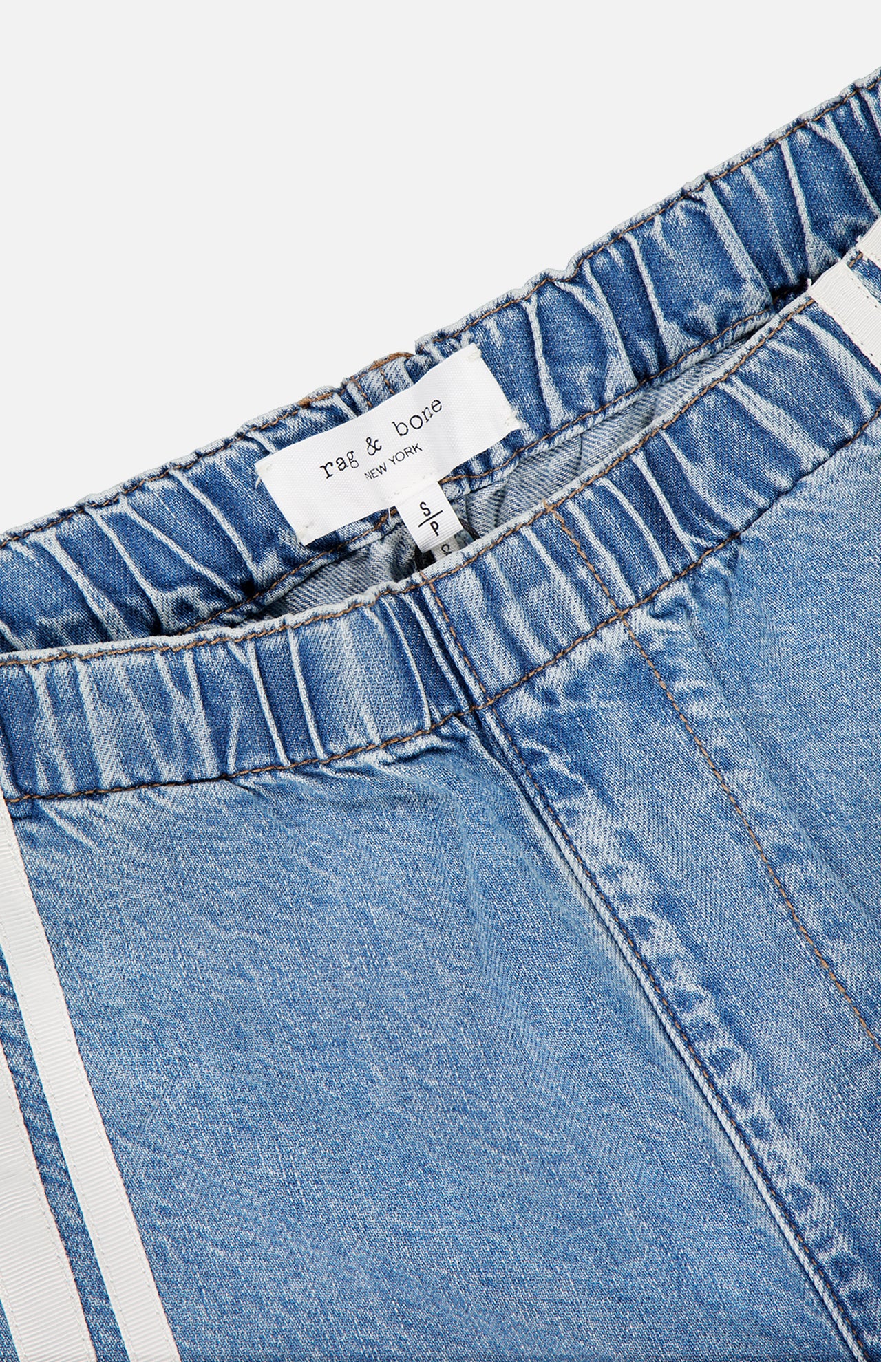 Close-up of the Featherweight Logan Track Pant in Eversport by RAG & BONE, featuring blue featherweight denim, elastic waistband, white side stripes, and a visible brand label. These relaxed track pants provide effortless style and comfort.