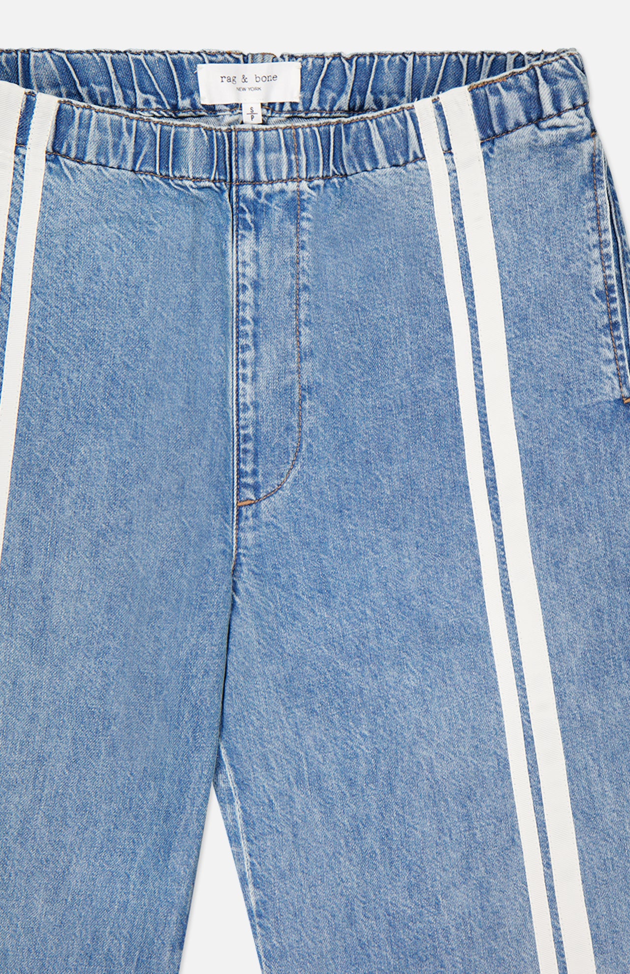 A close-up of light blue Featherweight Logan Track Pant in Eversport by RAG & BONE. These wide-leg pants feature an elastic waistband, vertical white side stripes, relaxed fit, visible stitching, and a signature brand label.