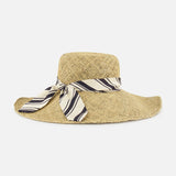 The RAG & BONE Garden Seagrass Hat with Scarf is a wide-brimmed summer hat, crafted from sea grass and adorned with a beige and black striped ribbon bow, shown on a plain white background.