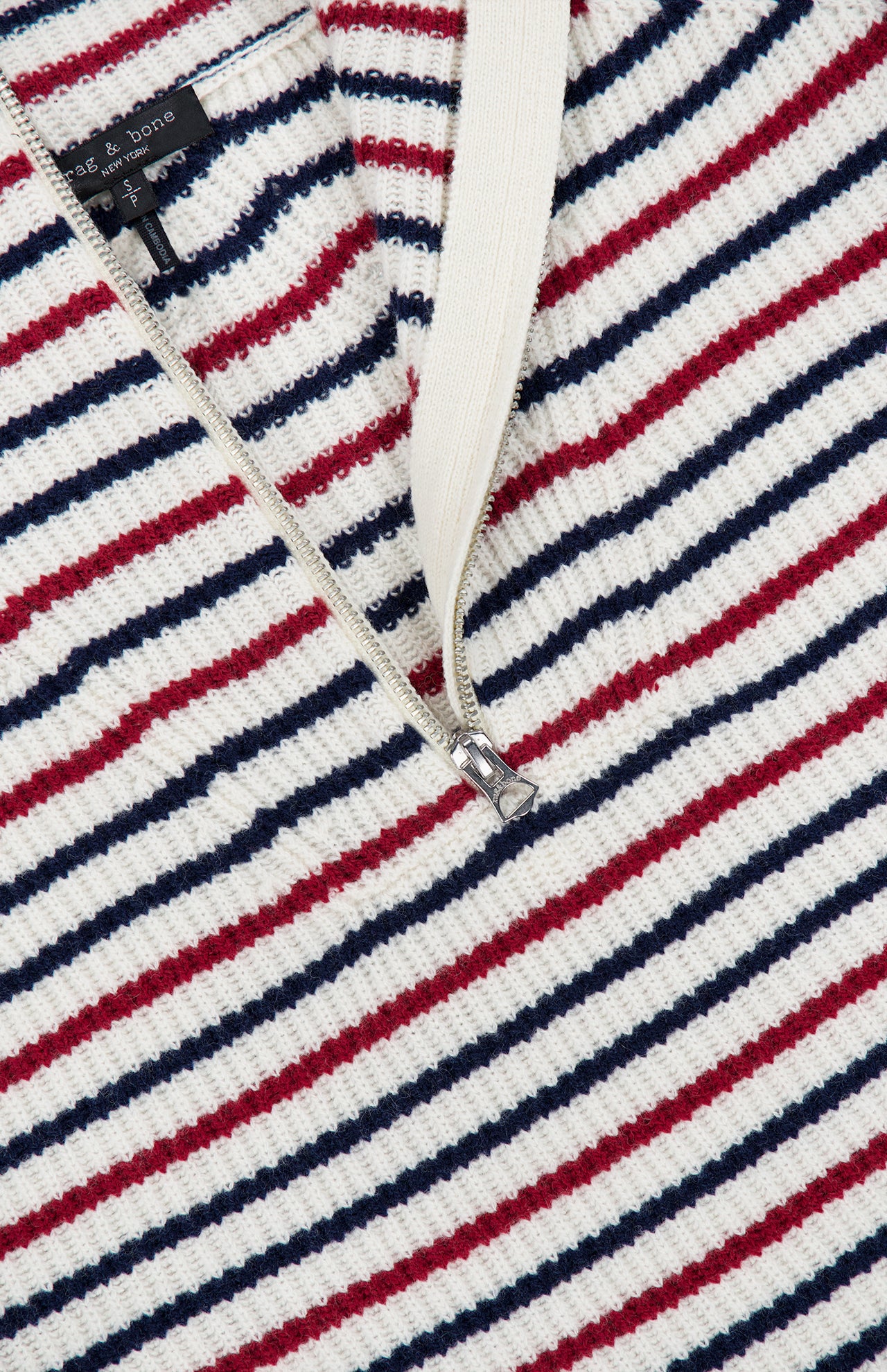 Close-up of the Georgie Stripe Half Zip Sweater by RAG & BONE—an ivory zip neck sweater with red, navy, and white stripes, ribbed texture, a crisp white collar, and partially unzipped silver zipper.