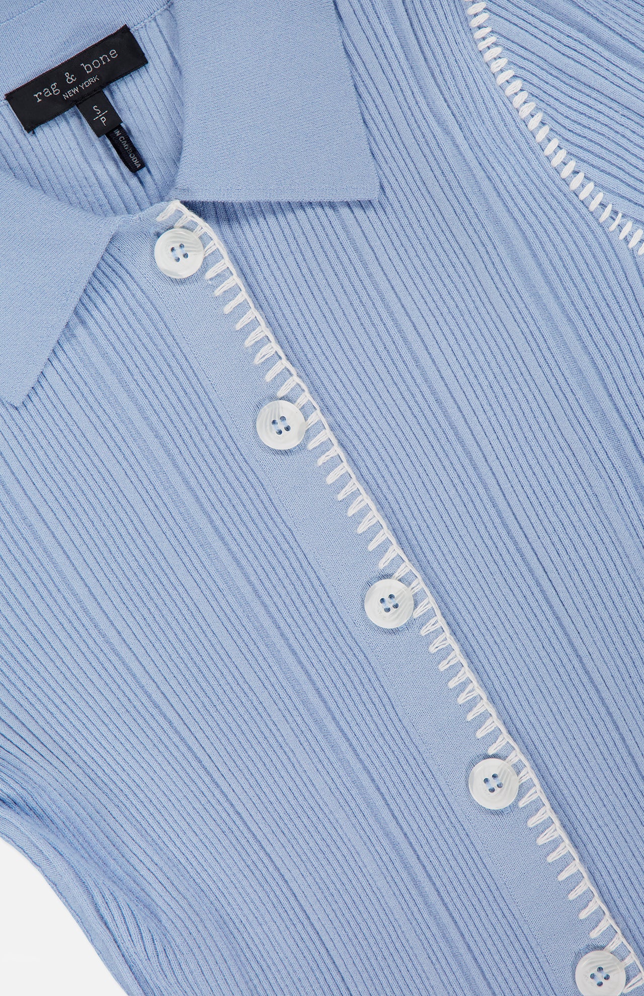 Close-up of the Harper Short Sleeve Cardigan Sweater by RAG & BONE in light blue, featuring a ribbed knit texture, white buttons, white decorative stitching on the placket, and a visible slim collar with the RAG & BONE tag.