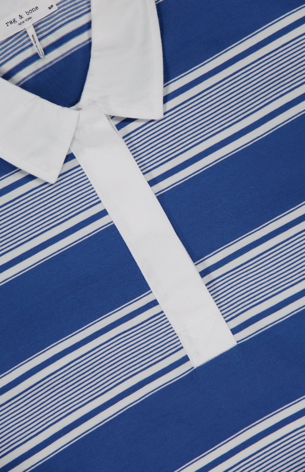 Close-up of the RAG & BONE Kelly Stripe Long Sleeve Polo Shirt, featuring blue and white horizontal stripes, a white collar, button placket, and visible neck label.