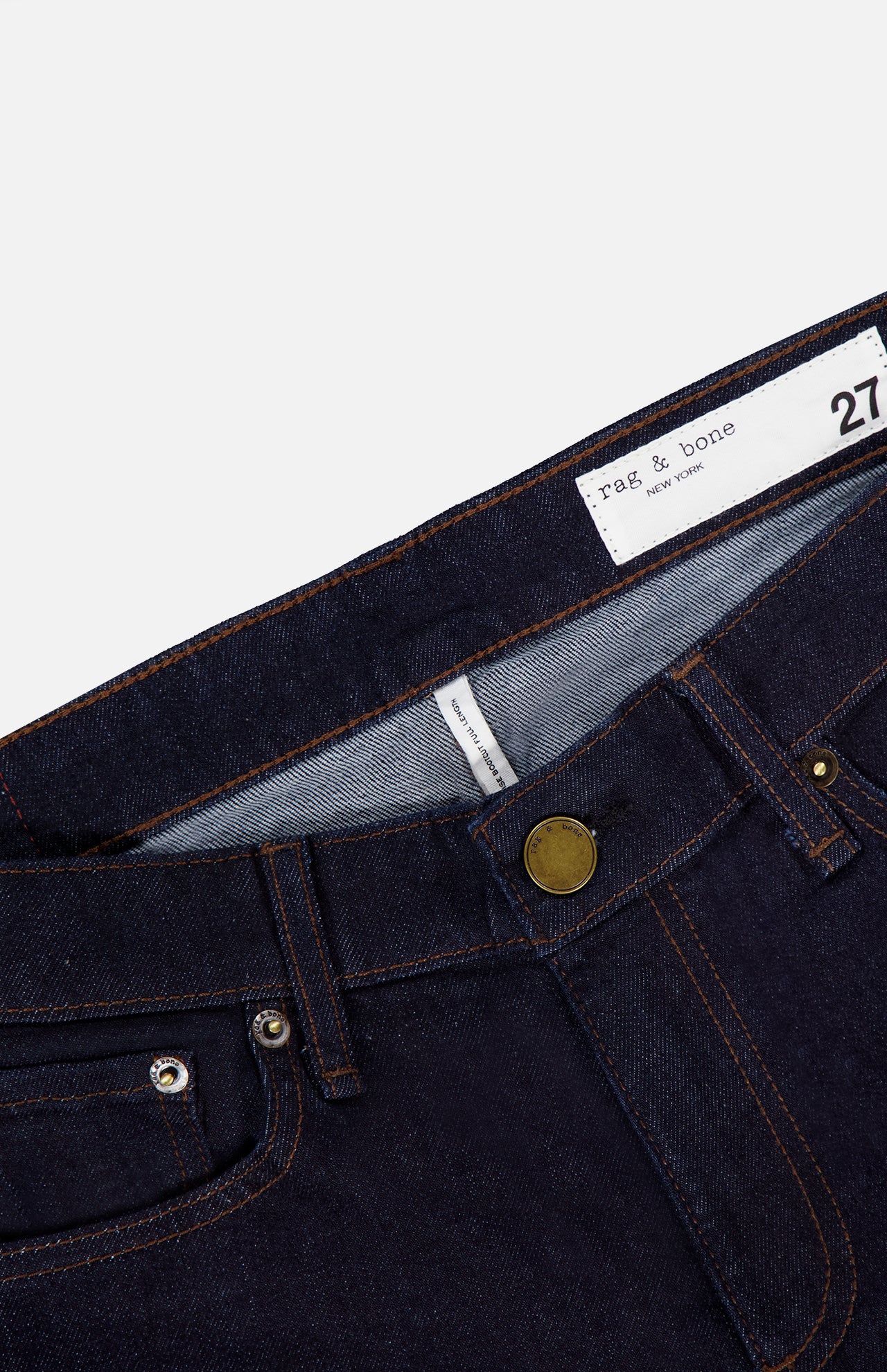 Close-up of a pair of RAG & BONE Kinsley Low Rise Full Bootcut Jeans in Dark Rinse, featuring stretch denim in dark blue, copper rivets, a brass button, front pockets, and a white waistband label displaying the brand name and size 27.