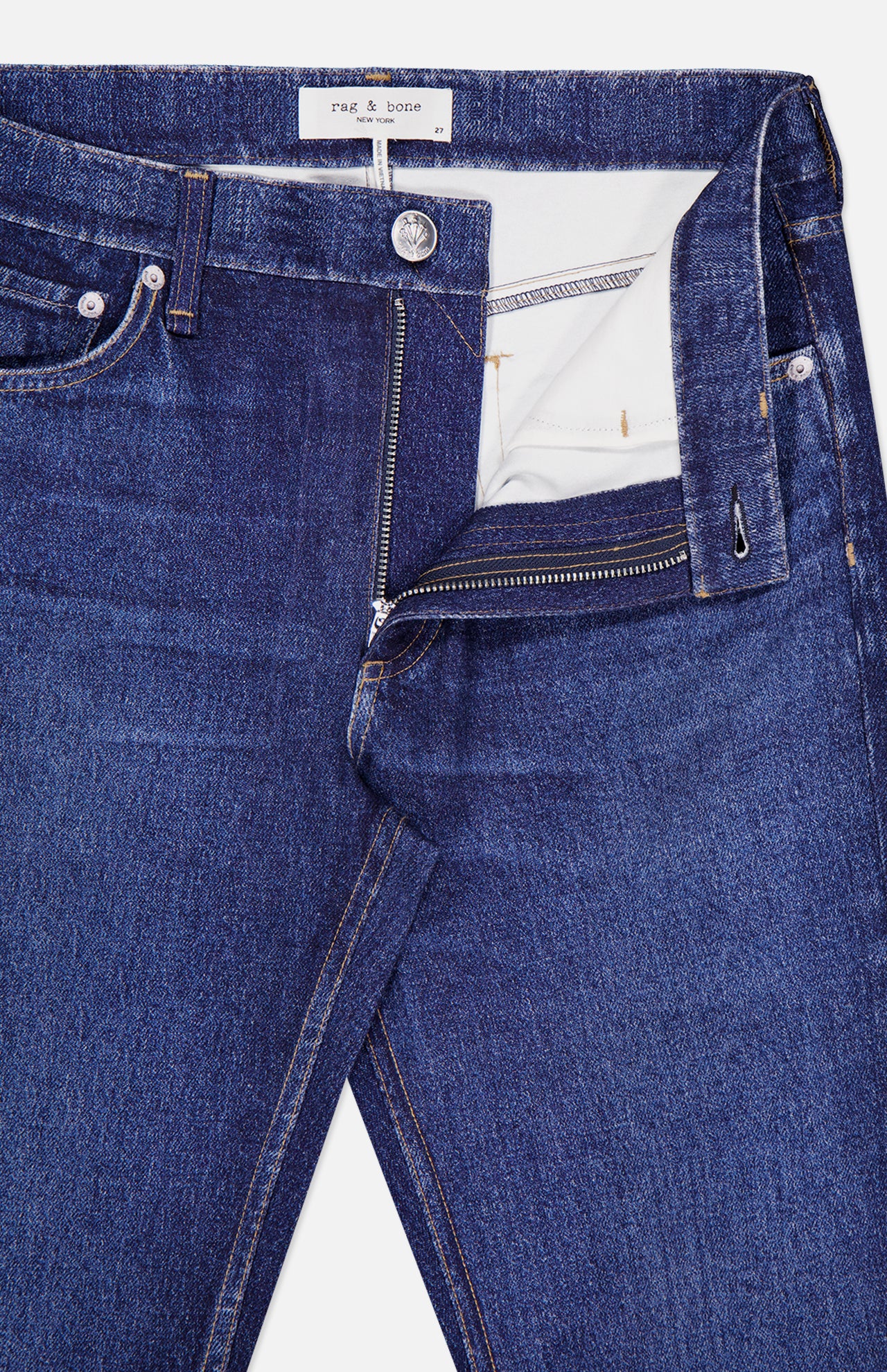 A close-up of the Miramar Ponte Dahlia Flare Jean in Nolita by RAG & BONE shows blue denim with a partially open zipper, revealing the waistband, button, and a white tag with RAG & BONE text inside. These jeans capture classic style with their signature denim print detailing.