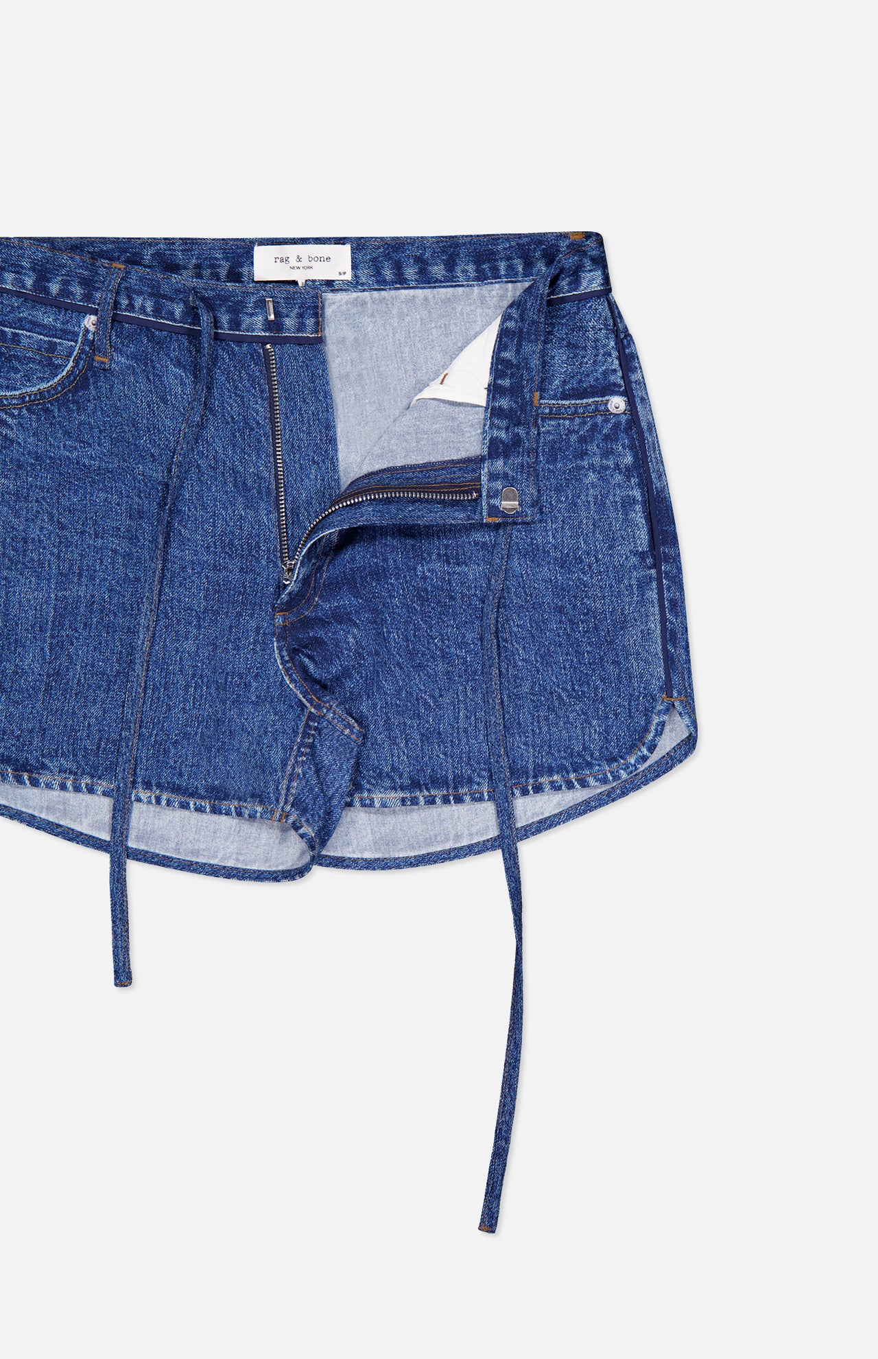 A close-up of RAG & BONE's Miramar Slink Lounge Short in York, blue denim with a drawstring waist and open zipper, laid flat on a white background.