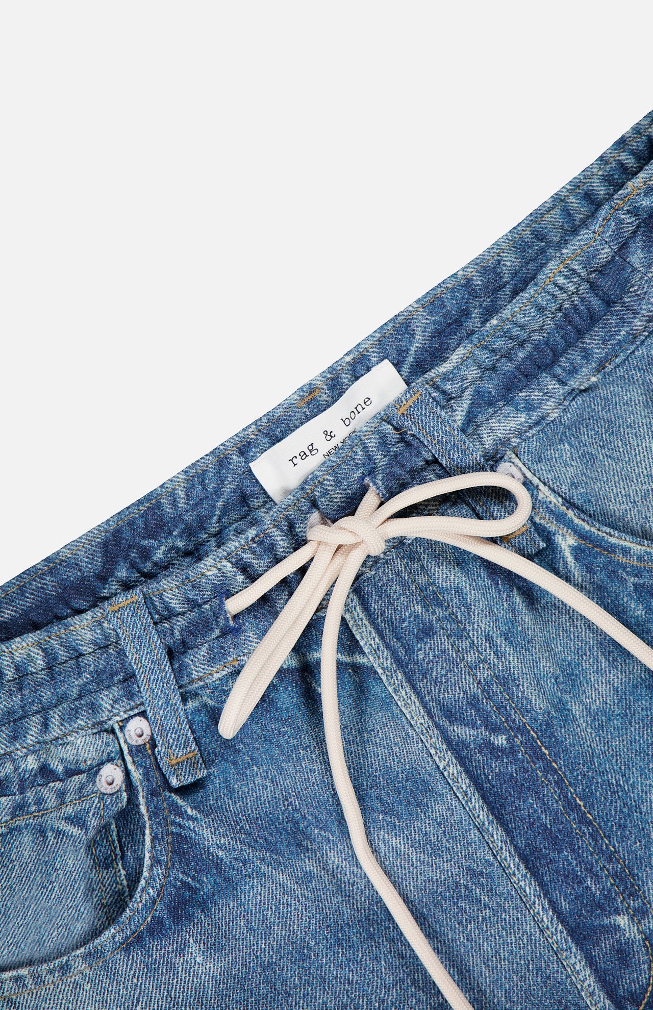 Close-up of the RAG & BONE Miramar Terry Drawstring Wide Leg Pant in Ellis, featuring a blue denim look, a white drawstring tied in a bow at the waist, and a visible rag & bone label sewn onto the inner waistband.