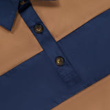 A close-up of the RAG & BONE Oversized Tie Hem Rugby Shirt, showcasing its tan and navy thick horizontal stripes, contrasting blue collar and button placket with two visible brown buttons, and classic long-sleeved polo styling.