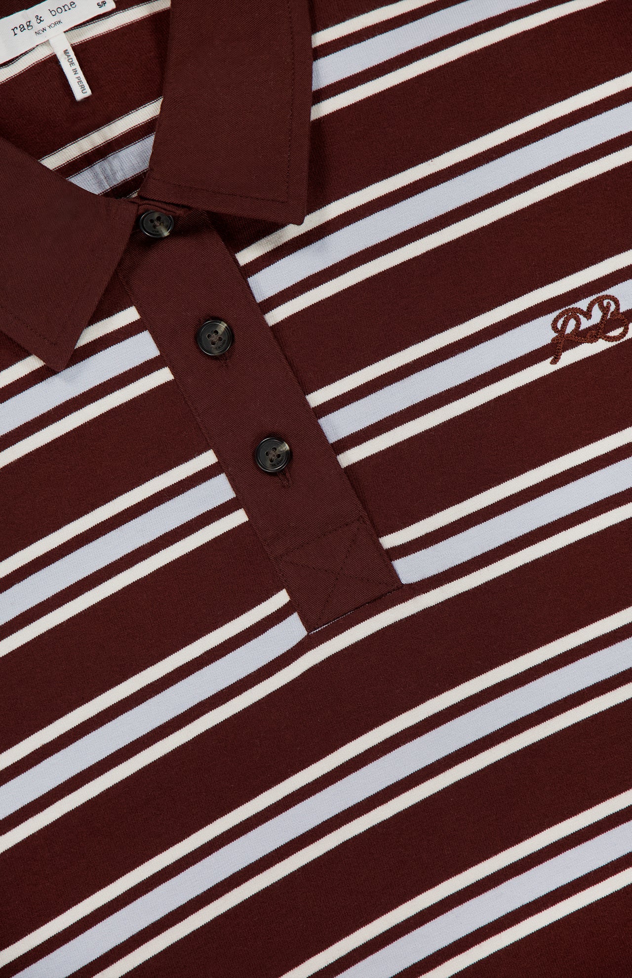 Close-up of a RAG & BONE Rugby Stripe Long Sleeve Shirt in maroon with white diagonal stripes, three black buttons, and an embroidered chest logo. The partially visible tag is near the collar.